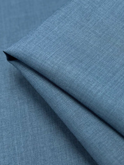 A close-up of Twill Suiting - Bluesteel by Super Cheap Fabrics shows neatly folded blue fabric with a smooth texture, fine diagonal weave, clean lines, and subtle shading.