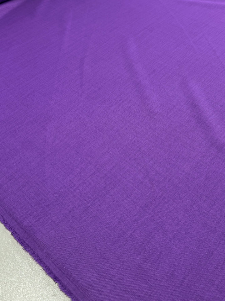 A close-up of Super Cheap Fabrics' Twill Suiting - Amethyst Orchid (150cm) shows bright purple polyester laid flat, revealing a subtle diagonal weave for added texture with gentle creases.