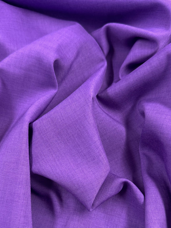 Close-up of Super Cheap Fabrics’ Twill Suiting - Amethyst Orchid (150cm), featuring bright purple polyester with soft folds, a smooth, slightly shiny finish, and a subtle diagonal weave.