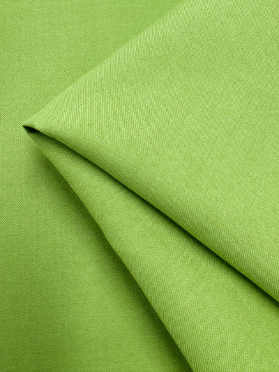 A close-up of Super Cheap Fabrics’ Twill Suiting - Green Glow (150cm), neatly folded to showcase its smooth polyester texture and fine diagonal weave, with soft diagonal lines formed by the fabric’s folds.
