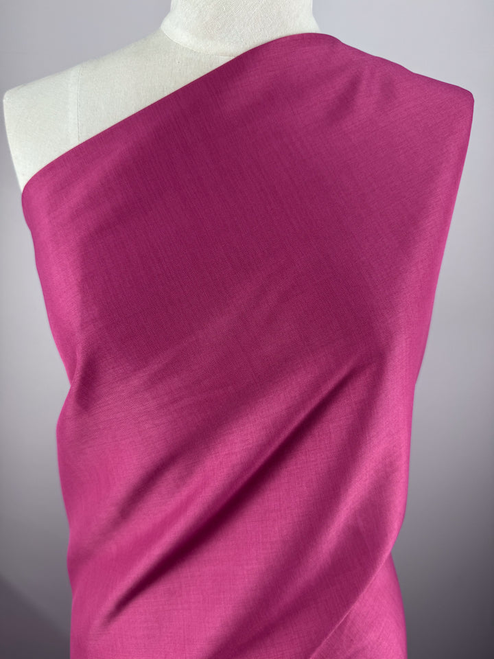 A mannequin showcases Super Cheap Fabrics' Twill Suiting - Fuchsia Rose - 150cm, elegantly draped over one shoulder to reveal its subtle diagonal weave, set against a plain light gray background.