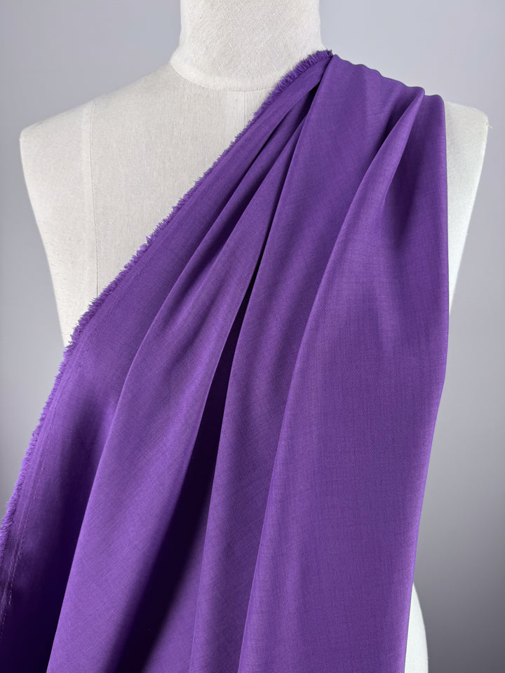 A mannequin showcases Super Cheap Fabrics' Twill Suiting - Amethyst Orchid - 150cm, featuring vibrant purple polyester with raw edges, set against a neutral gray background.