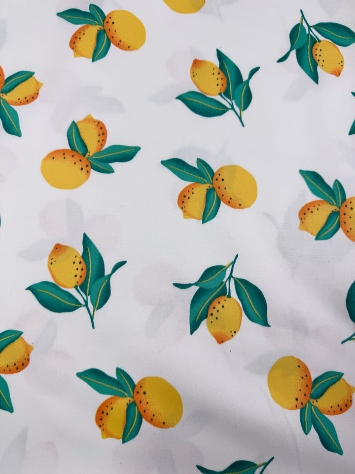 Super Cheap Fabrics’ Cotton Sateen - Lemon Grove (145cm) features white cotton fabric with a lively multi-colour pattern of yellow lemons and green leaves scattered across the surface.