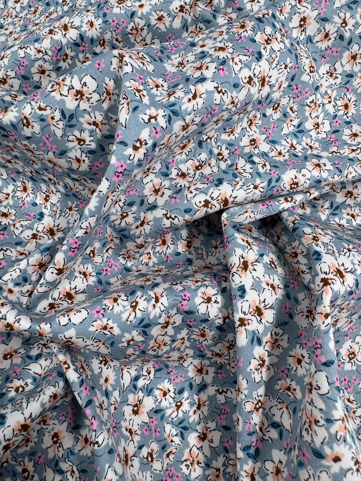 Super Cheap Fabrics' Cotton Sateen - Bluebell Meadows (150cm), a light blue fabric with densely packed white, brown, and pink florals plus foliage, is slightly wrinkled and softly folded—perfect for versatile sewing projects.