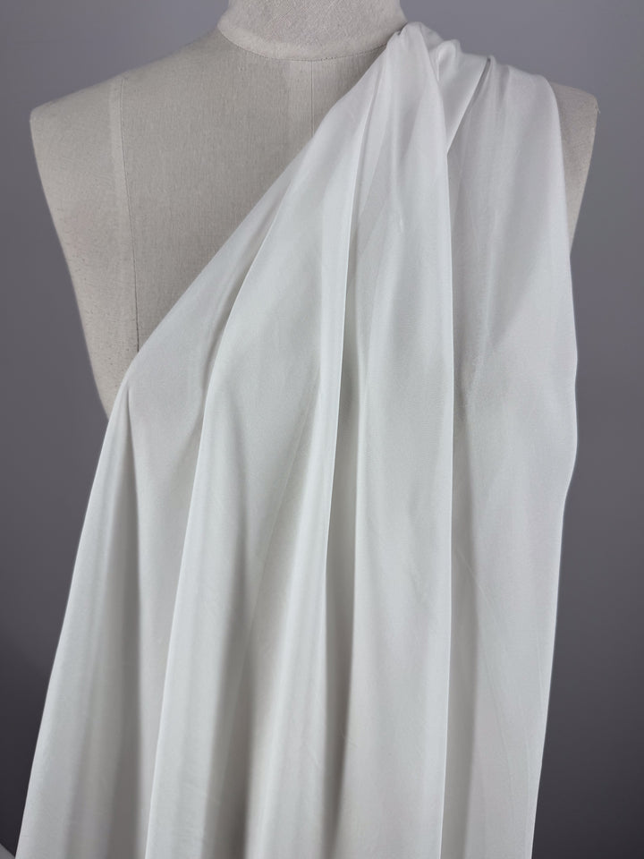 Super Cheap Fabrics' Pure Silk Chiffon - Ivory (140cm) is shown draped elegantly on a mannequin, covering one shoulder toga-style with soft, flowing folds—ideal for creating light spring and summer looks.