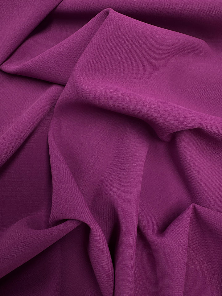 The Microfibre Suiting - Purple Wine - 150cm from Super Cheap Fabrics features a smooth, lightweight surface, shown draped and folded to create soft ripples and gentle shadows across its luxurious polyester fabric.