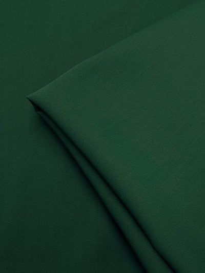 A close-up of Super Cheap Fabrics’ Microfibre Suiting in Dark Green (150cm), showing the lightweight polyester’s smooth surface and subtle texture as it rests folded on a matching background.
