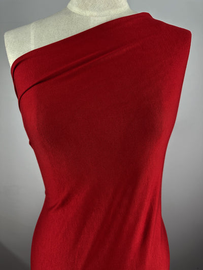 A mannequin draped in a vibrant red Rayon Lycra - Salsa - 145cm by Super Cheap Fabrics that covers one shoulder, with the other shoulder and arm visible. The smooth, medium weight fabric highlights the curves of the mannequin against a plain gray background, adding an elegant touch to the overall presentation.