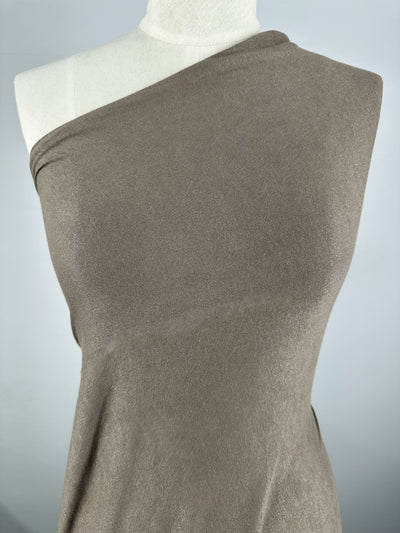 A close-up view of a Linen Knit - Smokey Olive - 150cm by Super Cheap Fabrics draped on a dress form against a neutral gray background. The lightweight fabric appears to have generous stretch, wrapping smoothly around the torso with a simple, elegant design.