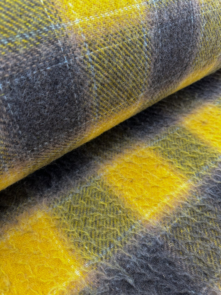 Here is a close-up of Virgin Wool - Spruzzo from Super Cheap Fabrics, a heavy weight wool fabric featuring a plaid pattern in shades of yellow and gray. The soft, fuzzy texture of this 145cm wide virgin wool material is perfect for overcoats, showcasing alternating squares with subtle variations in tone and weave.