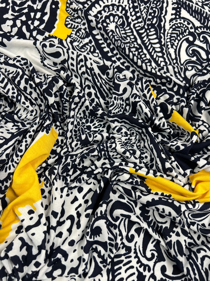 A close-up of intricately patterned black and white Printed Lycra - Mandala - 150cm by Super Cheap Fabrics with splashes of yellow. The design includes abstract shapes and motifs, suggestive of paisley and floral elements, with the medium weight fabric appearing to be loosely gathered.