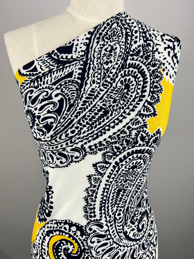 A sleeveless dress on a mannequin showcases a bold paisley print in black, white, and yellow. Made from Super Cheap Fabrics' Printed Lycra - Mandala - 150cm, it creates a striking and modern design against the plain gray background.