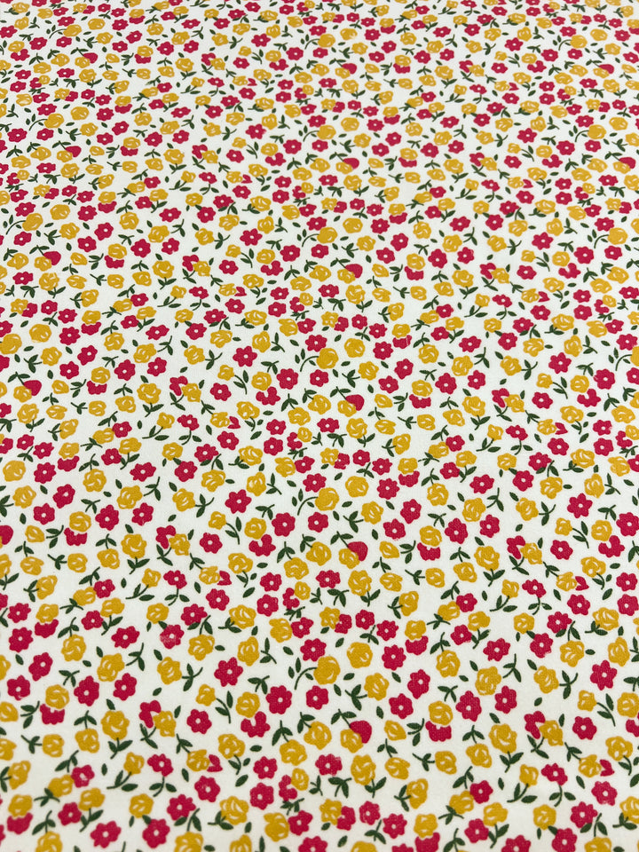 A patterned cotton fabric featuring a dense arrangement of small floral designs, reminiscent of an Autumn garden. The flowers are primarily red and yellow, with green leaves, all set on a white background. The pattern is evenly distributed across the entire fabric surface. This is the Printed Pinwale Corduroy - Poppy - 145cm from Super Cheap Fabrics.