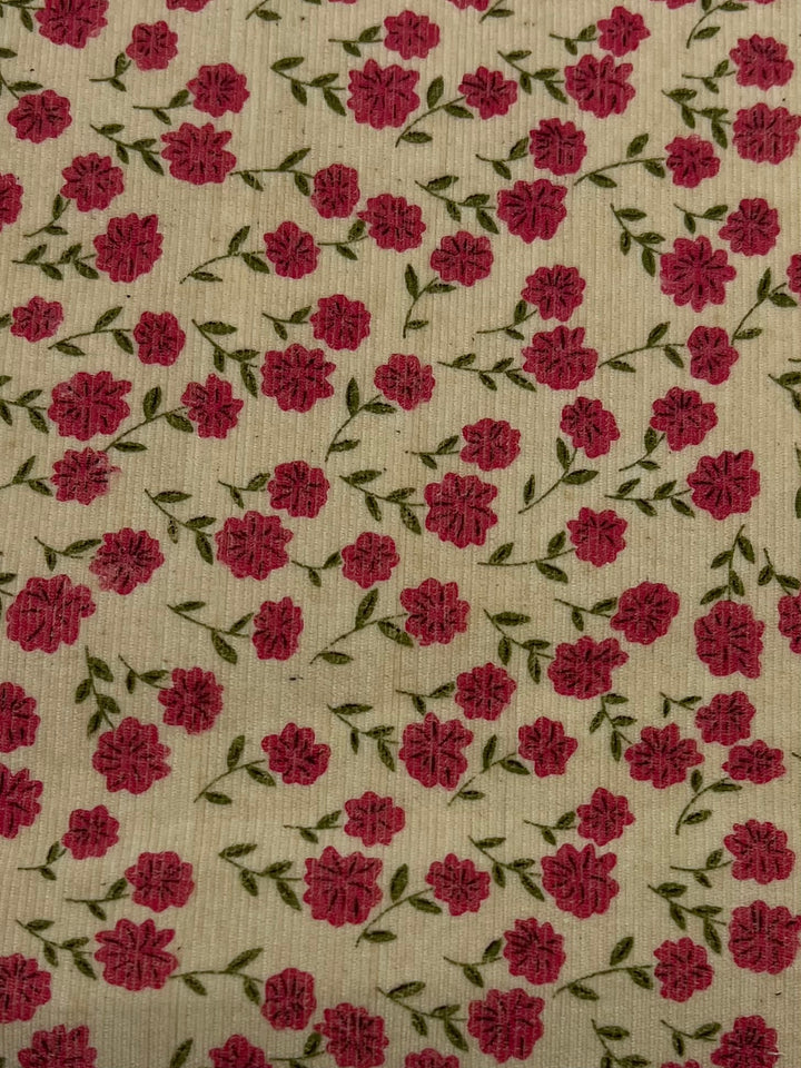 A home decor fabric pattern featuring small, bright pink flowers with green leaves scattered across a cream-colored background. The design is repetitive, creating a uniform floral texture with evenly spaced blossoms and foliage. This is the Printed Micro Corduroy - Autumn Garden - 150cm by Super Cheap Fabrics.