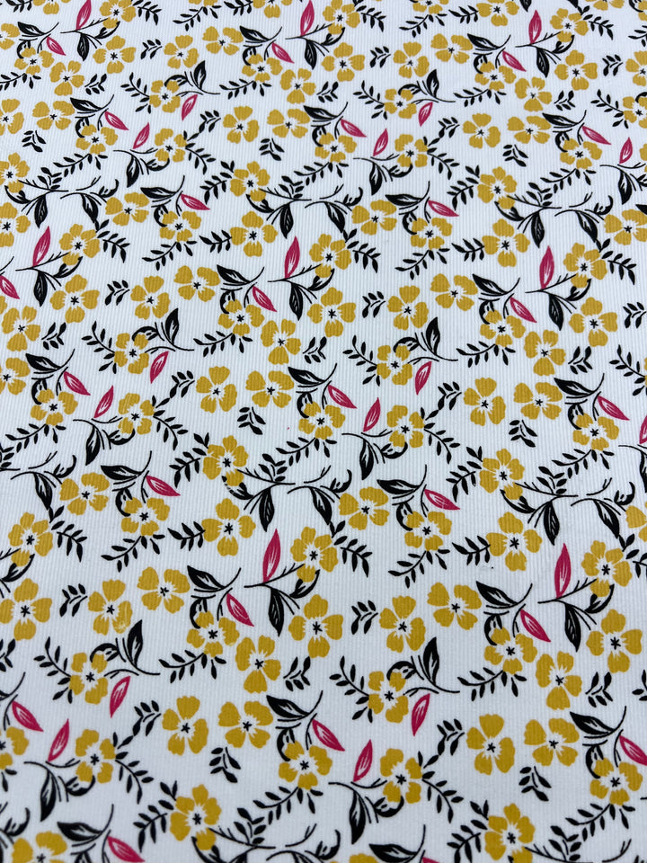 The Super Cheap Fabrics Printed Micro Corduroy - Sprung - 145cm features a repetitive pattern of small yellow flowers, black leaves, and pink petals. The background is white with subtle gray lines running vertically, creating a delicate and intricate Autumn garden design perfect for home decor.