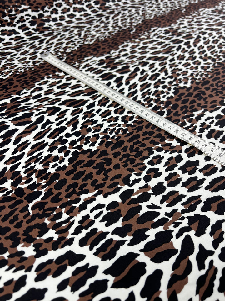 A close-up shot of a brown, black, and white leopard print design on lightweight cotton fabric. A measuring tape is placed on top, displaying centimeter measurements—perfect for household décor projects. This is the Cotton Sateen - Striped Leopard - 148cm by Super Cheap Fabrics.