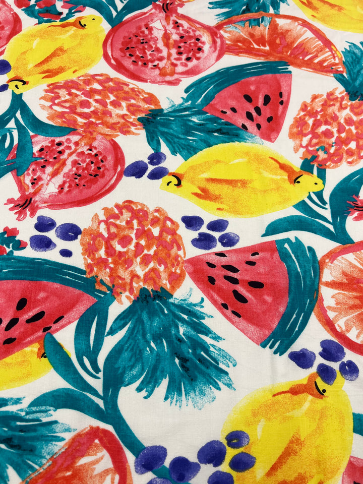 A colorful fabric pattern featuring illustrated pomegranates, pineapples, watermelons, lemons, and blueberries against a white background. The vibrant design showcases a tropical and summery theme with bold and vivid colors, including red, yellow, green, and blue—perfect for lightweight bamboo rayon projects like the Bamboo Rayon - Fiesta - 150cm from Super Cheap Fabrics.