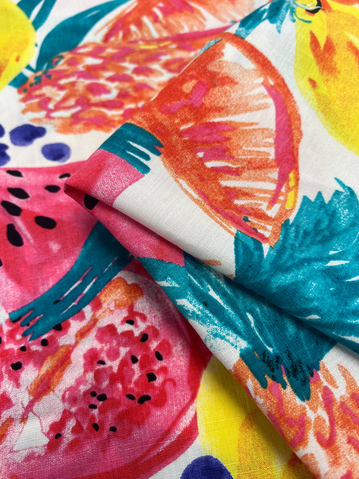 Close-up image of colorful, tropical-patterned Bamboo Rayon - Fiesta - 150cm by Super Cheap Fabrics featuring bright illustrations of fruits like watermelon, lemons, and citrus slices in vibrant hues of pink, yellow, green, and blue. The lightweight fabric shows folds, enhancing the textural detail.