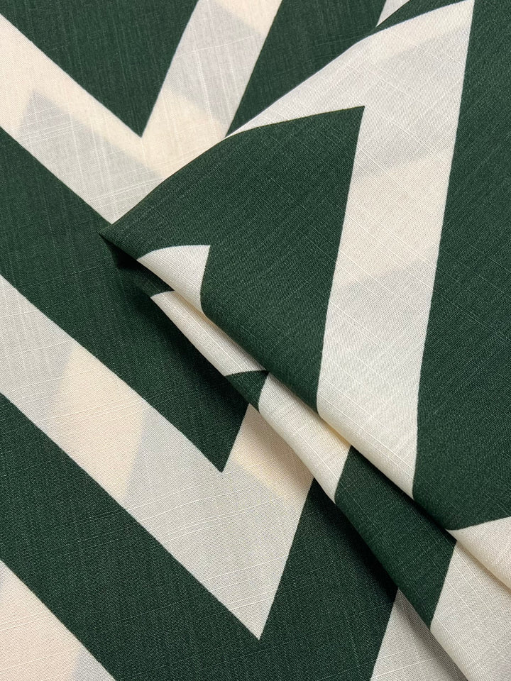 A close-up of folded fabric with a green and white geometric zigzag pattern. The lightweight fabric appears to be made of smooth Bamboo Rayon - Zag XL - 150cm from Super Cheap Fabrics, featuring clean, sharp lines in the design. Ideal for versatile uses, this material promises elegance and comfort.
