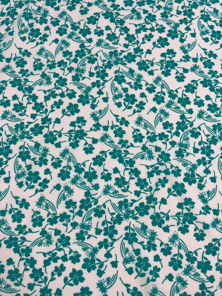 A lightweight fabric with a green floral pattern on a white background. The design features clusters of small flowers and leaves, creating an intricate, repetitive motif that's perfect for Super Cheap Fabrics Bamboo Rayon - Aqua Ditsy - 150cm garments.