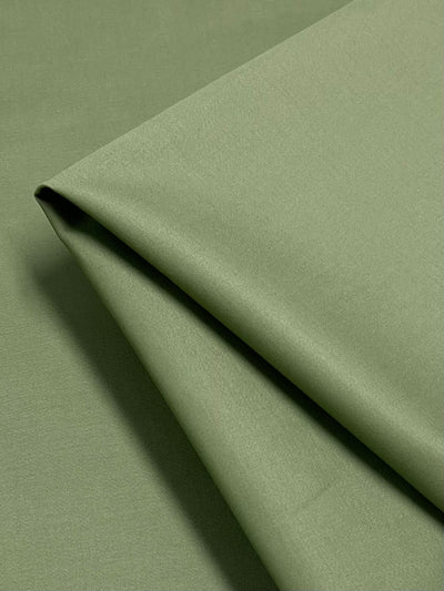 A close-up of a neatly folded piece of Super Cheap Fabrics' Plain Sateen - White Pear - 148cm showcases a smooth and matte texture. The fabric has a slight sheen, and the folds create subtle, clean lines that highlight its softness and quality—ideal for sophisticated workwear.