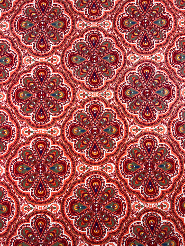 An intricately designed, soft fabric features a repeating pattern of red and maroon floral shapes. Each petal-like formation is filled with detailed motifs in shades of green, orange, and brown, over a white background that adds contrast to the vibrant design. This multiuse textile boasts a high-quality print. Introducing the Printed Nylon Lycra - Mirage - 150cm from Super Cheap Fabrics.