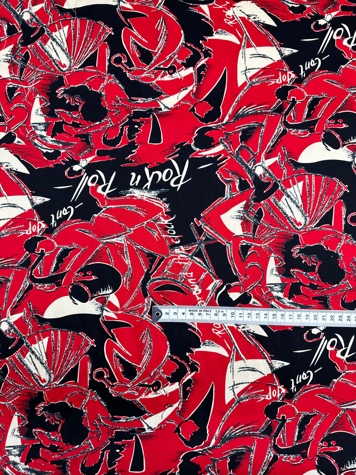A vibrant piece of cotton fabric is designed with red, black, and white abstract patterns, featuring silhouettes of dancers, musical notes, and the phrase "Rock 'n' Roll." A white measuring tape spans across the lightweight fabric, making it perfect for household decor. The product name is Cotton Sateen - Rock Roses - 150cm by Super Cheap Fabrics.