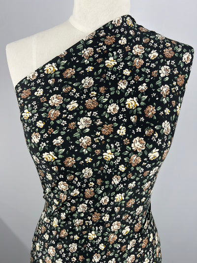 A one-shoulder dress with a black background and a floral pattern featuring brown, white, and yellow flowers. Made from medium weight fabric, this Super Cheap Fabrics Printed Lycra - Spring Night - 150cm dress is displayed on a white mannequin.