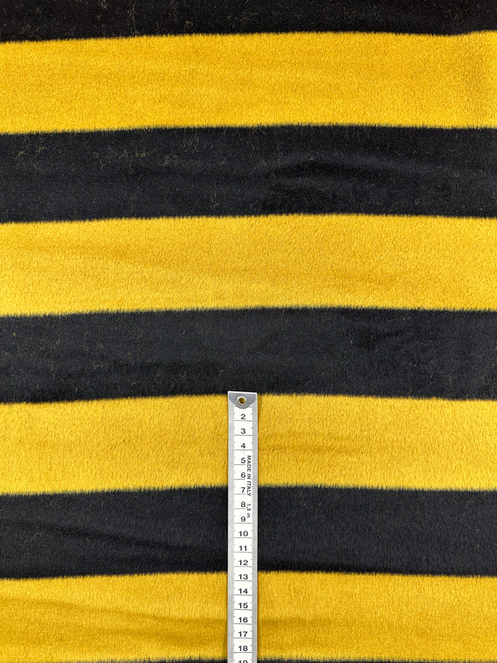 A close-up of Super Cheap Fabrics' Wool Cashmere - Honey shows luxurious, bee-patterned stripes in yellow and black. A ruler placed vertically measures from 9 to 18 cm, highlighting its premium 154cm width for year-round use.