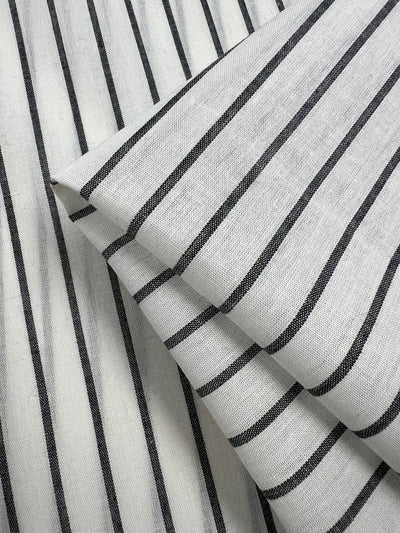 Folded pieces of durable fabric with vertical black stripes. The stripes are evenly spaced and run parallel across the Linen Cotton - Pin Charcoal and White Stripe - 145cm by Super Cheap Fabrics, giving it a clean and organized appearance. The texture of the fabric is slightly textured, adding depth to the natural fibers' pattern.