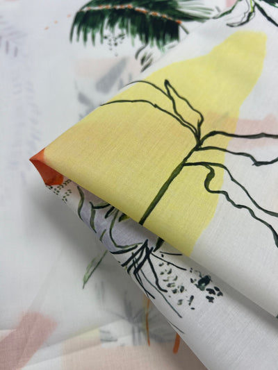 A close-up of folded Designer Cotton - Holiday - 136cm width cotton fabric by Super Cheap Fabrics featuring a botanical design. The lightweight fabric showcases a yellow abstract background with black line drawings of flowers and leaves. The cloth appears soft, with overlapping layers that highlight the delicate pattern, ideal as multi-use fabric.