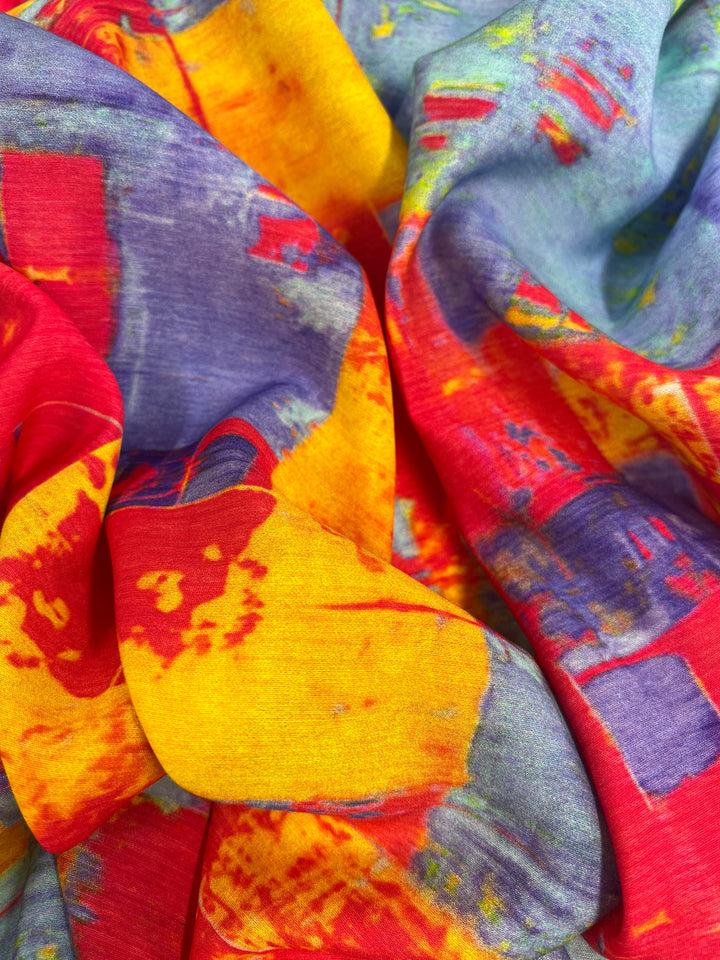 A close-up image of a vibrant, multicolored fabric featuring abstract patterns. This lightweight Designer Cotton - Fire and Ice - 145cm by Super Cheap Fabrics showcases a blend of bright red, yellow, blue, and green hues with a slightly crumpled texture, creating a dynamic and eye-catching visual.