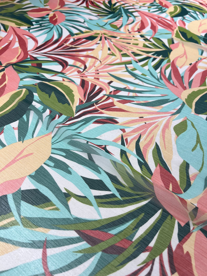 A vibrant fabric pattern featuring an array of overlapping tropical leaves in pastel shades of pink, turquoise, green, and yellow. This extra lightweight "Designer Chiffon - Paradise - 150cm" from Super Cheap Fabrics is perfect for fancy dresses or adding a lively touch to home décor with its intricate design and mix of large and small leaves.