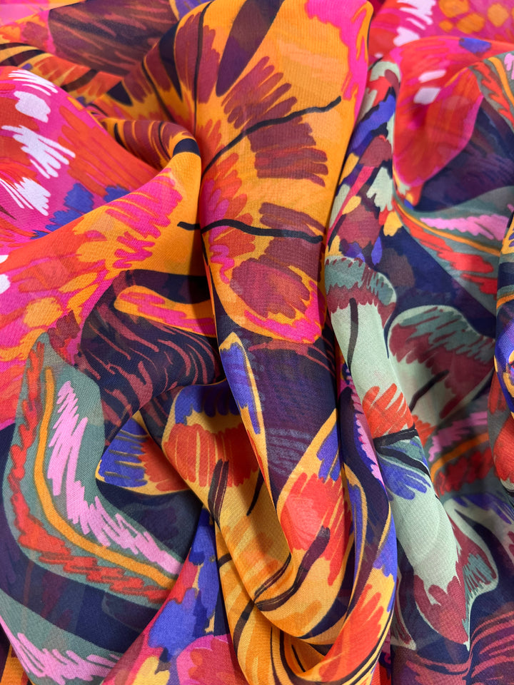 A vibrant and colorful fabric with an intricate pattern of abstract shapes and brush strokes, ideal for fancy dresses. The design features a mix of red, orange, purple, pink, and blue hues, creating a lively, dynamic aesthetic. The fabric has folds and an extra lightweight texture that's sheer and graceful. This is the Designer Chiffon - Wonderland - 150cm by Super Cheap Fabrics.