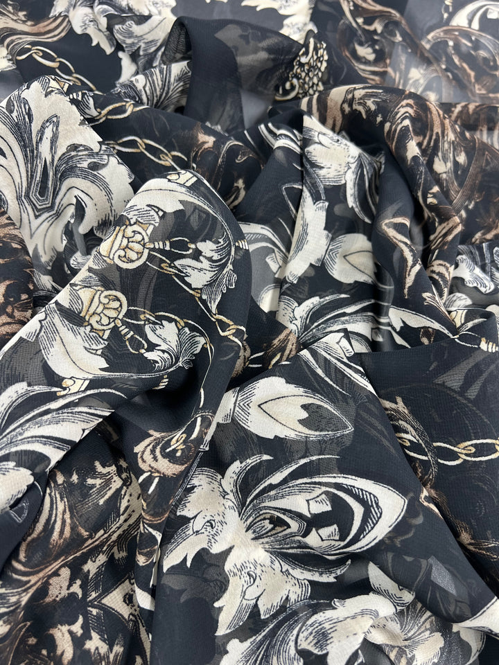 A close-up of Super Cheap Fabrics' Designer Chiffon - Cathedral Chains - 150cm, an extra light weight fabric with a complex baroque pattern. The fabric features black, white, and beige floral and chain designs, creating a rich, opulent texture perfect for home décor. The material appears soft and slightly sheer.