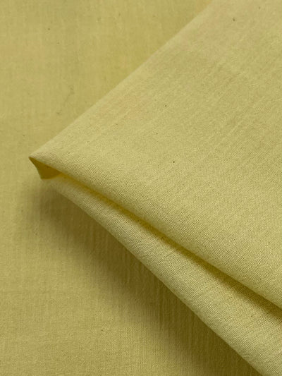 A close-up of Super Cheap Fabrics Cotton Gauze - Yellow - 138cm, folded neatly with visible texture and slight creases, indicating a smooth, lightweight material perfect for children's clothing.