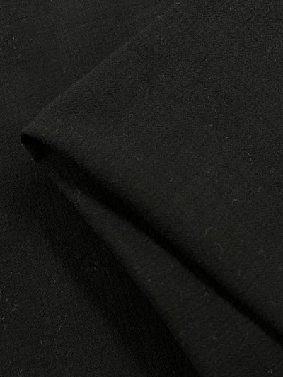 A close-up image of lightweight Cotton Gauze - Black - 112cm from Super Cheap Fabrics folded at an angle, showing its texture and thickness. The 100% cotton material appears smooth and slightly matte, with minor lint or fibers visible on the surface.