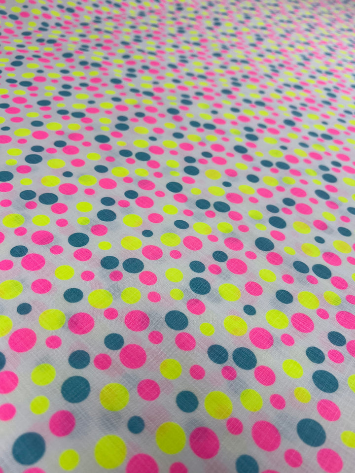 A close-up image of a white Linen Cotton - Spotty - 150cm by Super Cheap Fabrics adorned with a vibrant pattern of multicolored polka dots in bright shades of pink, yellow, and blue, creating a lively and cheerful design. The breathable fabric is crafted from natural fibers for added comfort.