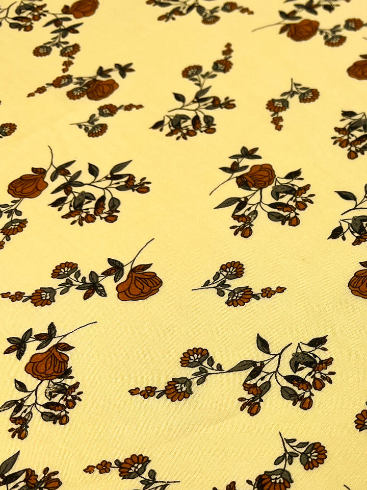 A Super Cheap Fabrics Printed Rayon - Calico Flor - 145cm with a yellow background is adorned with a repeating pattern of small floral bunches. The flowers are predominantly in shades of brown and dark green, with delicate stems and leaves enhancing the natural and intricate design, making it a versatile choice for various projects.