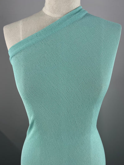 A Lightweight Slub Jersey - Aqua - 150cm displayed on a mannequin against a dark gray background. The fabric is fitted and features textured knit for maximum comfort, available from Super Cheap Fabrics.