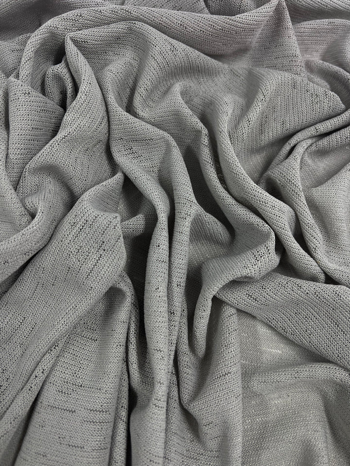 A close-up view of crumpled, light gray fabric with a textured pattern. The folds and wrinkles create shadows that add depth to the material. The weave appears delicate and slightly sheer, embodying maximum comfort while showcasing unique designs from Super Cheap Fabrics' Lightweight Slub Jersey - Light Grey - 150cm.
