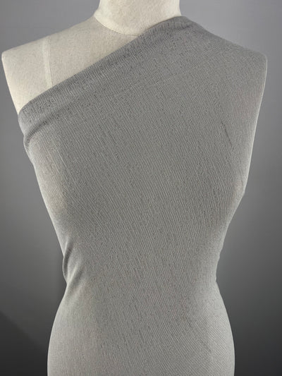 A mannequin torso displays a gray, one-shoulder, sleeveless top crafted from Super Cheap Fabrics' Lightweight Slub Jersey - Light Grey - 150cm. The form-fitting material drapes smoothly over the mannequin's form. The background is a plain, dark gray color.