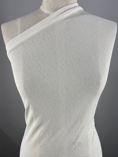 A close-up image of a mannequin draped in *Lightweight Slub Jersey - Ivory - 150cm* by *Super Cheap Fabrics*, set against a gray background. The versatile clothing fabric has a subtle pattern and fits snugly around the mannequin's torso.
