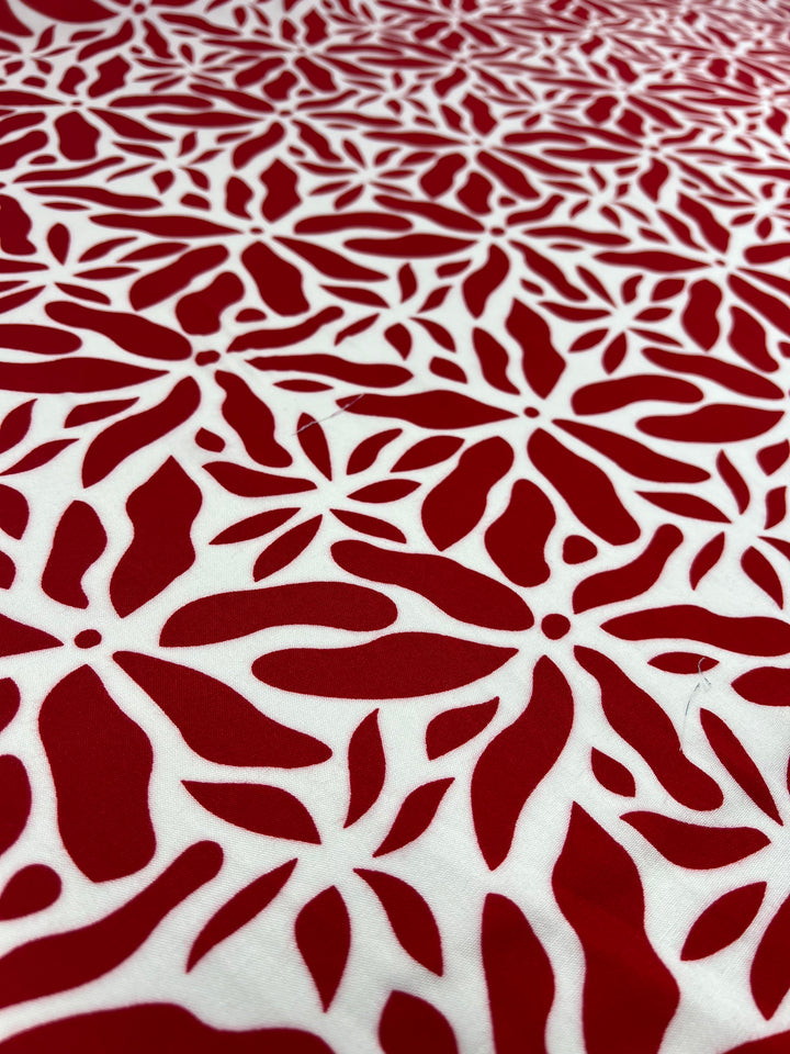 A close-up view of a Super Cheap Fabrics Designer Rayon - Scarlet - 140cm with a red and white floral pattern. The design consists of various red flower shapes and petals on a white background, creating a visually striking and intricate motif, perfect for those seeking versatile fabric options with vibrant prints.