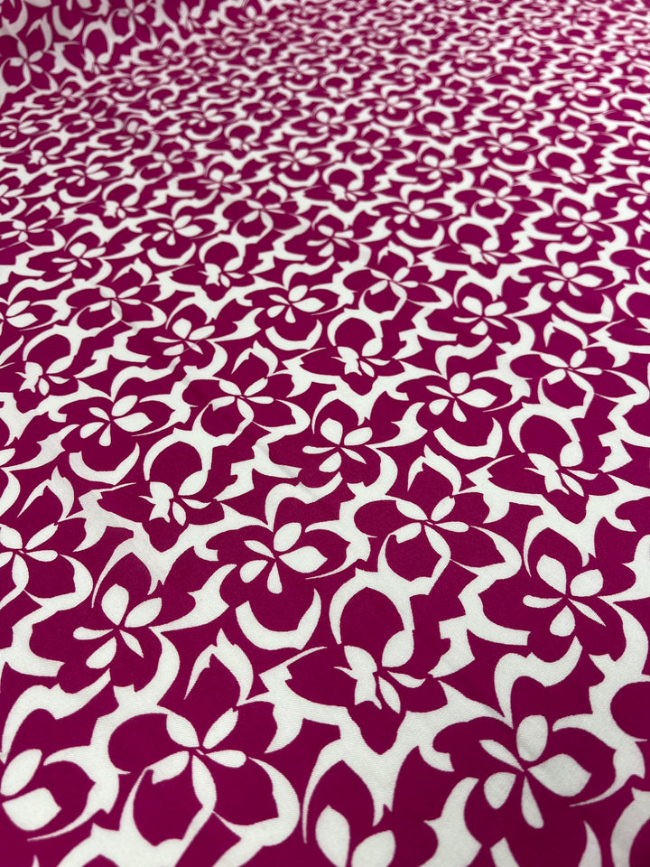 A close-up view of a versatile choice: vibrant prints featuring bold magenta flowers on a white Designer Rayon - Fuchsia - 140cm fabric background from Super Cheap Fabrics. The floral pattern showcases varying shapes and sizes, creating a visually dynamic and intricate design.