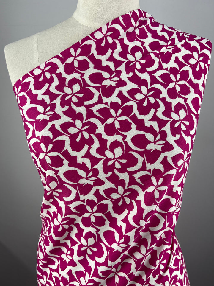 A mannequin draped with versatile Designer Rayon - Fuchsia - 140cm from Super Cheap Fabrics adorned with a bold pink floral pattern. The flowers are evenly distributed, creating a striking contrast against the white background. The vibrant prints are arranged to cover the mannequin's torso asymmetrically.