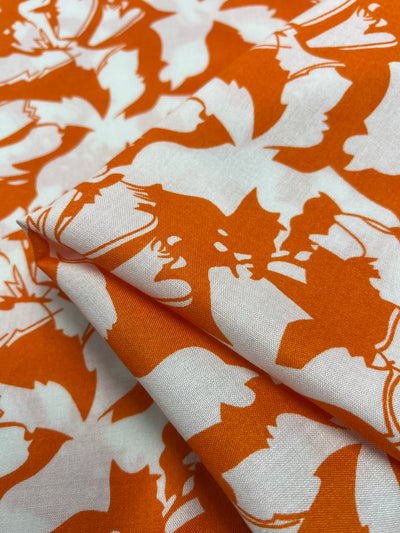 A close-up image of Super Cheap Fabrics' Designer Rayon - Tangelo - 140cm featuring a white fabric with a vivid orange bat pattern. Soft creases and shadows accentuate the bold contrast, highlighting the vibrant prints and making this versatile fabric perfect for any creative project.