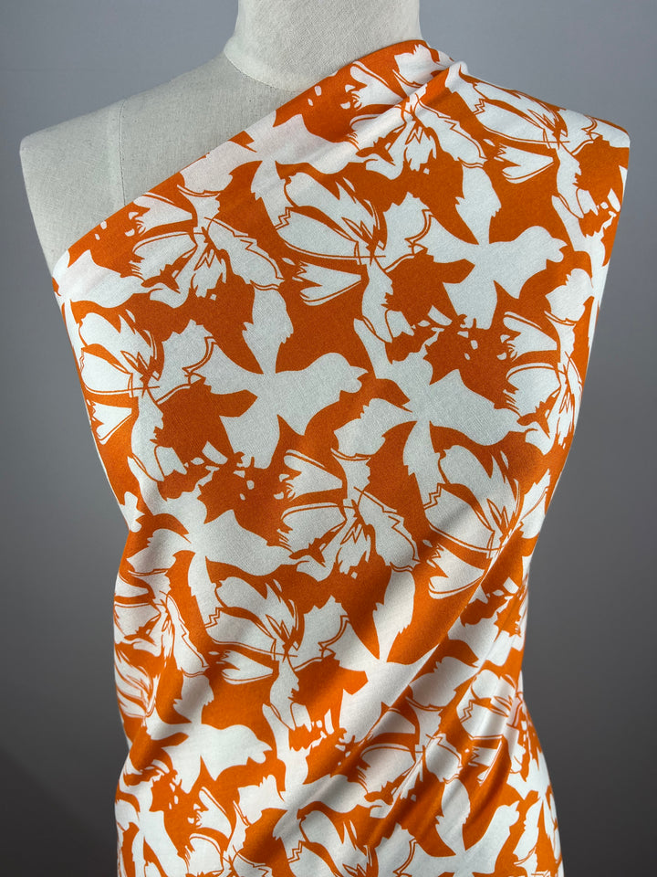 A dress form draped with vibrant prints in orange and white fabric featuring a bold bat pattern. The versatile Super Cheap Fabrics Designer Rayon - Tangelo - 140cm is wrapped asymmetrically across the form, highlighting the contrasting bat silhouettes against the energetic background.