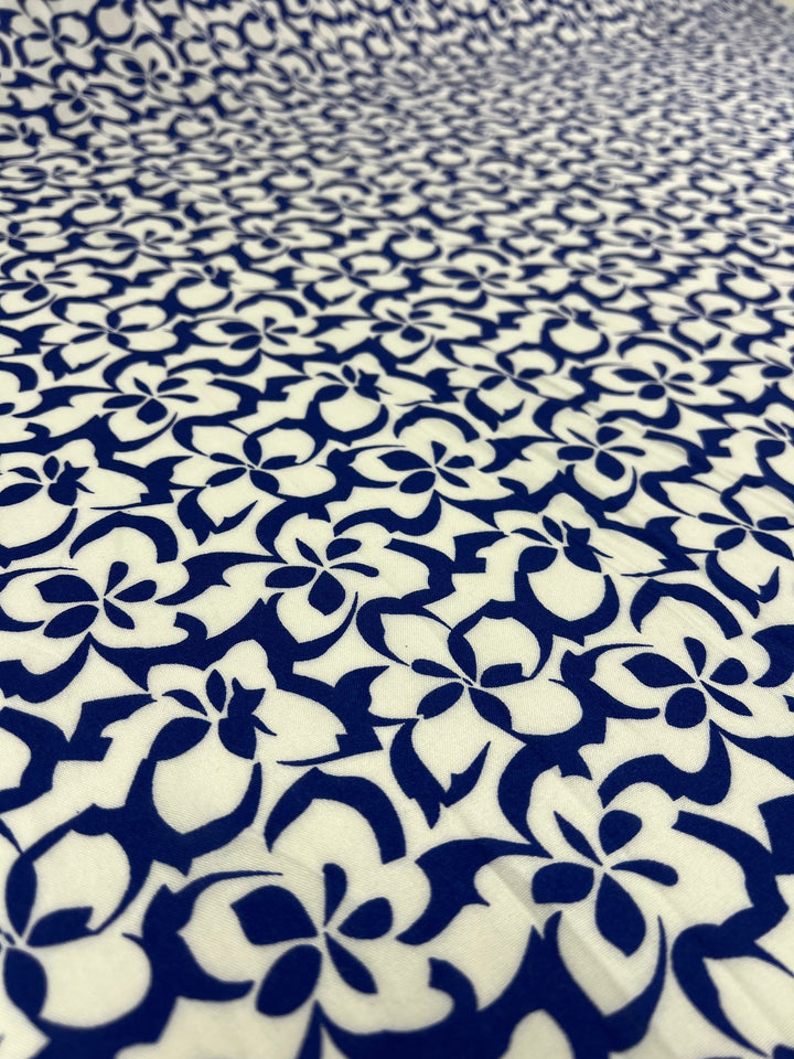 A close-up of Super Cheap Fabrics' Designer Rayon - Ultramarine - 140cm with a repeating pattern of abstract, flower-like shapes in blue on a white background. The design creates a dense and visually intricate texture, making it perfect for vibrant prints.