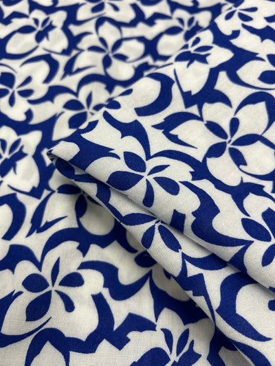 A close-up of Designer Rayon - Ultramarine - 140cm by Super Cheap Fabrics featuring a vibrant blue and white floral pattern. The design consists of abstract, connected flowers in blue against a white background. Part of the versatile fabric is folded to display its texture and design details more clearly.